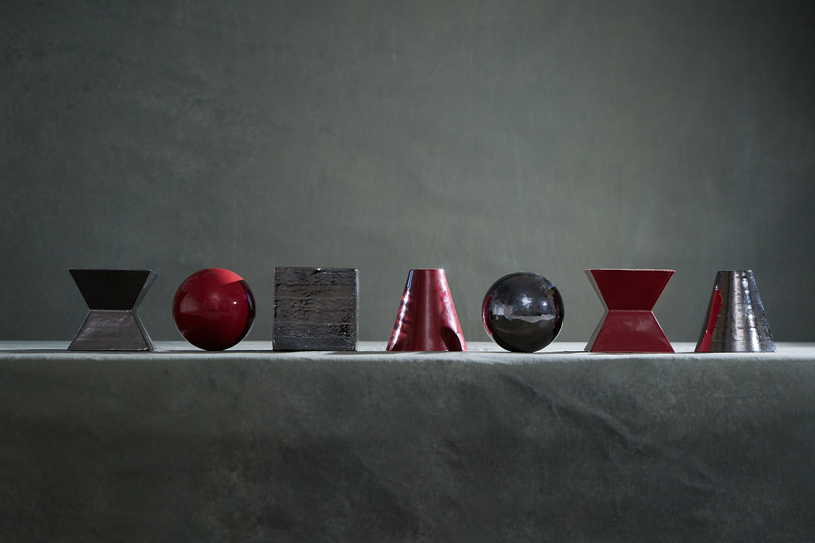 Row of geometric ceramic objects in black, red and steel